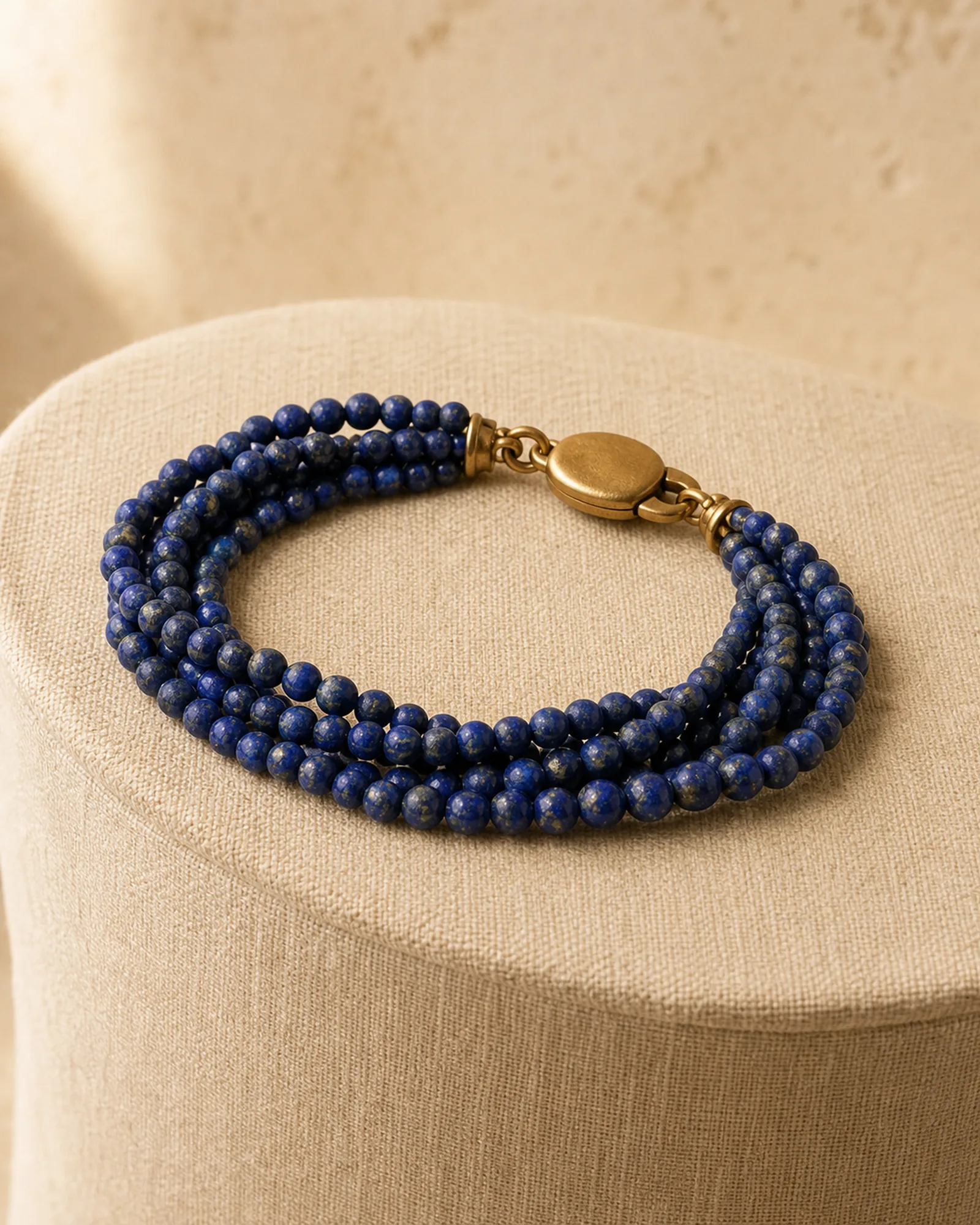Editorial mockup of a layered blue-bead bracelet on an oatmeal linen form